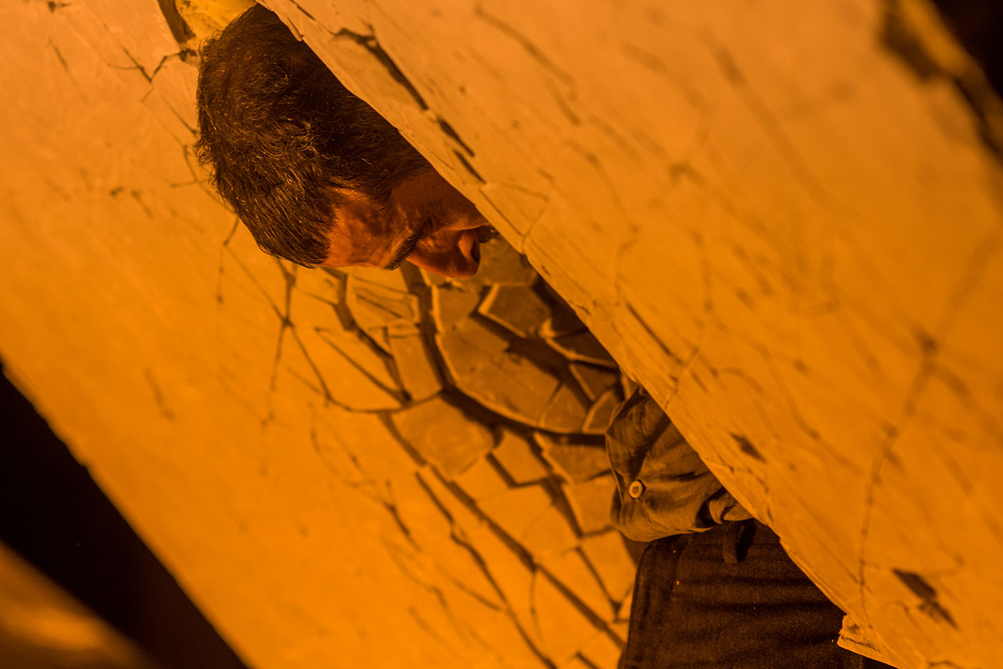 Person leaning against cracked wall, orange lighting