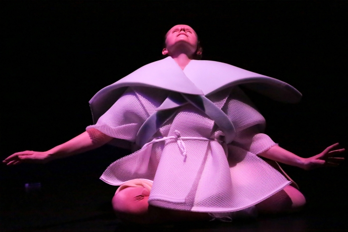 Performer in abstract costume on dark stage expressing art.
