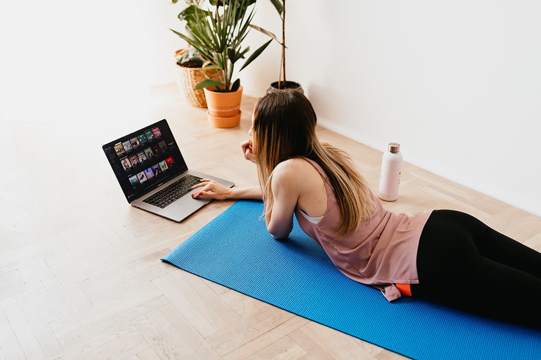 Young woman lying on yoga mat looking at her laptop