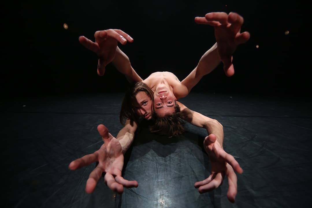 Two dancers performing on a dark stage.