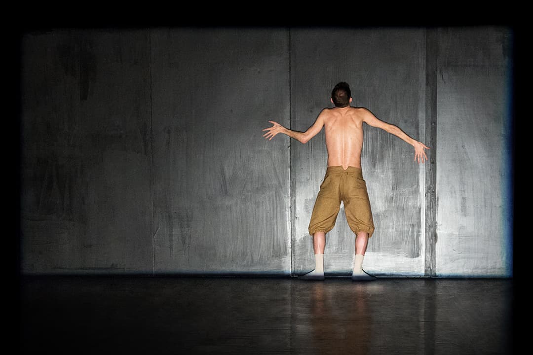 Person standing against dark wall in artistic pose.
