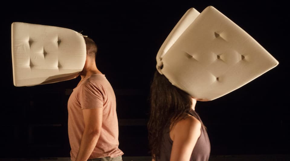 People wearing large cushions on their heads, black background.
