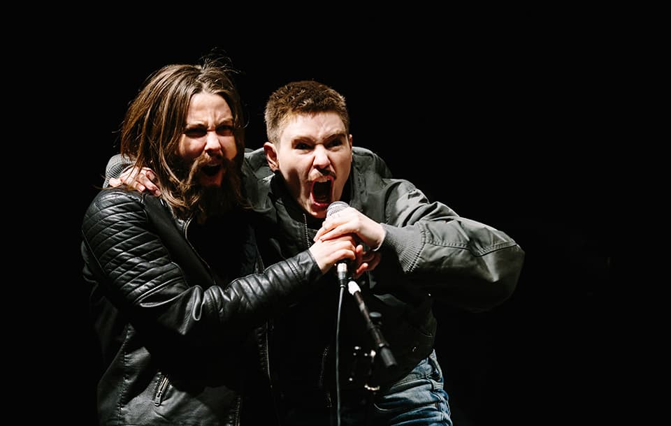 Two rock singers sharing a microphone on stage.