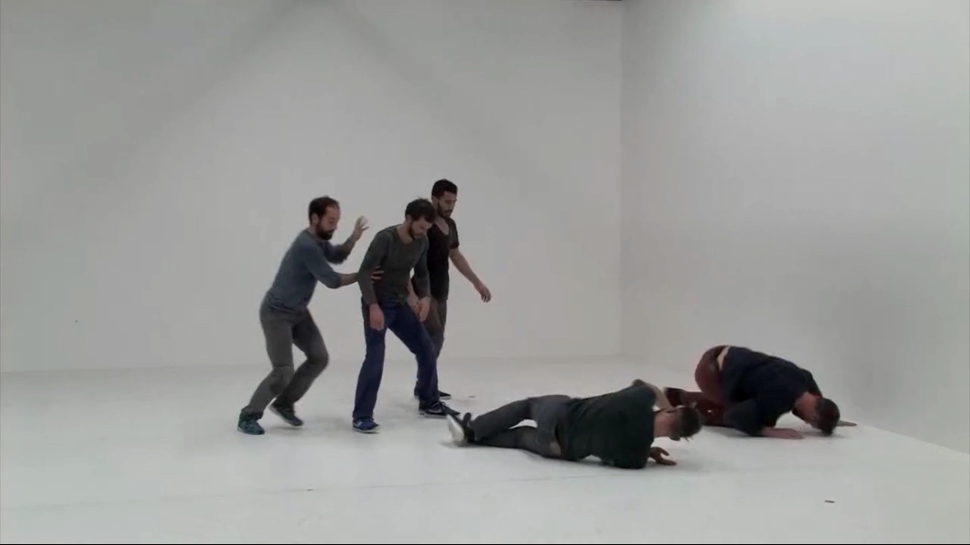 Five men in grey room, some crawling, some standing.