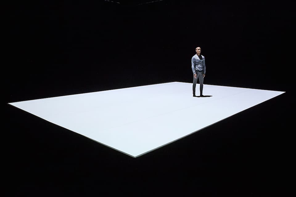 Person stands on illuminated stage in dark space.