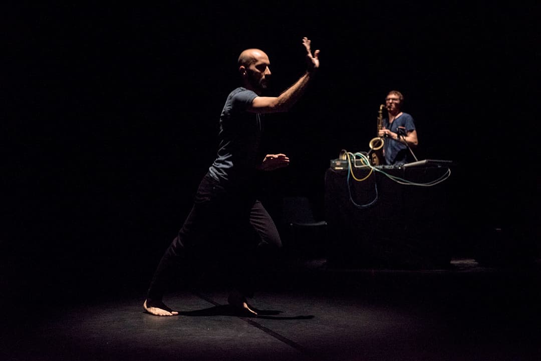 Performer dancing with musician playing saxophone on stage.