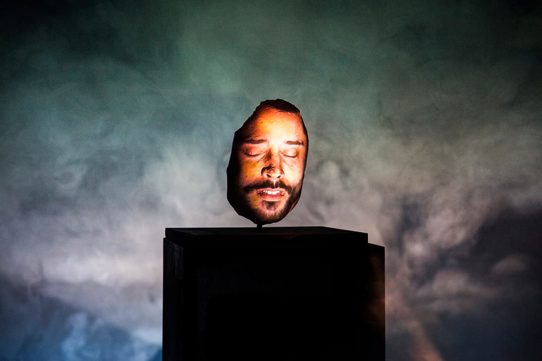 Illuminated head sculpture on a pedestal, cloudy background.