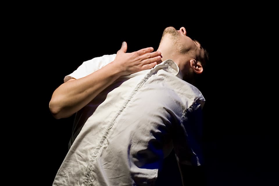Person in dramatic pose, white shirt, dark background.