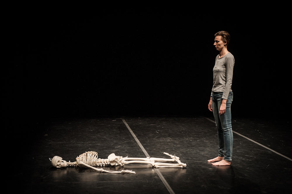 Woman standing next to human skeleton on stage.