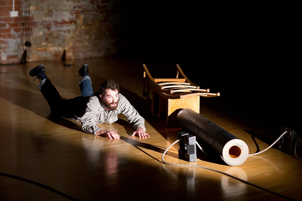 Man crawling toward overturned chair in dimly lit room.
