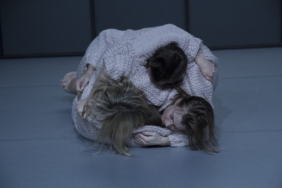 Group embracing on grey floor in sweaters.