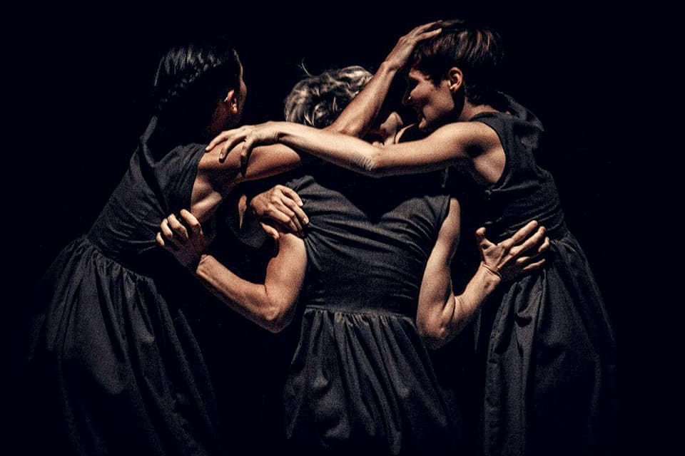 Three dancers embrace in a dramatic performance.