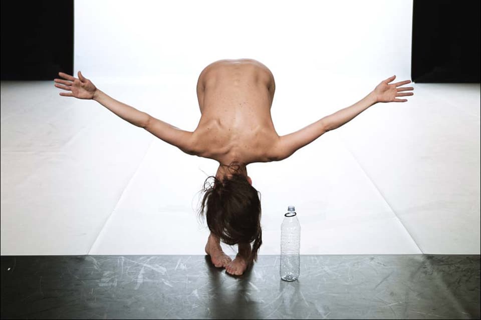Person bent over, arms outstretched, next to bottle.