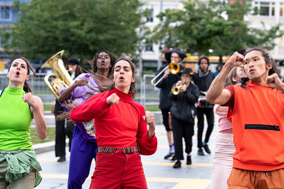 Dancers performing energetically with musicians outdoors.
