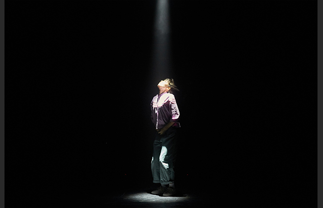Person illuminated by spotlight on dark stage.