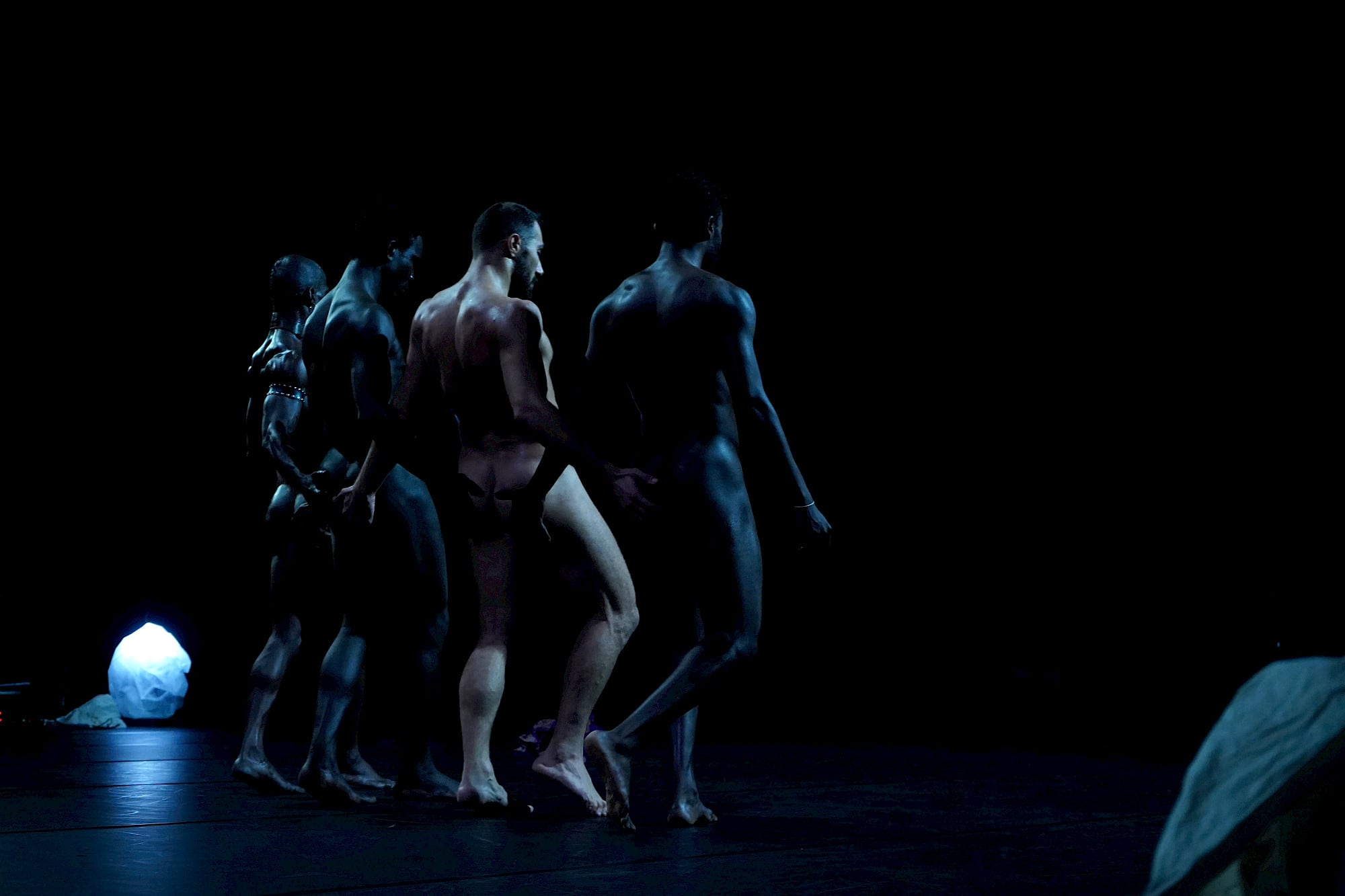 Four naked muscular men, backs towards us, joined in a row by hand-to-buttock links