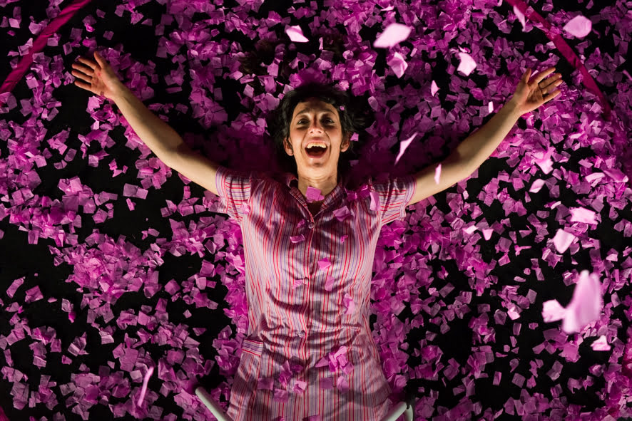 Topshot of woman in pink-purple tunic dress lying with arms open and smiling face on purple confetti background