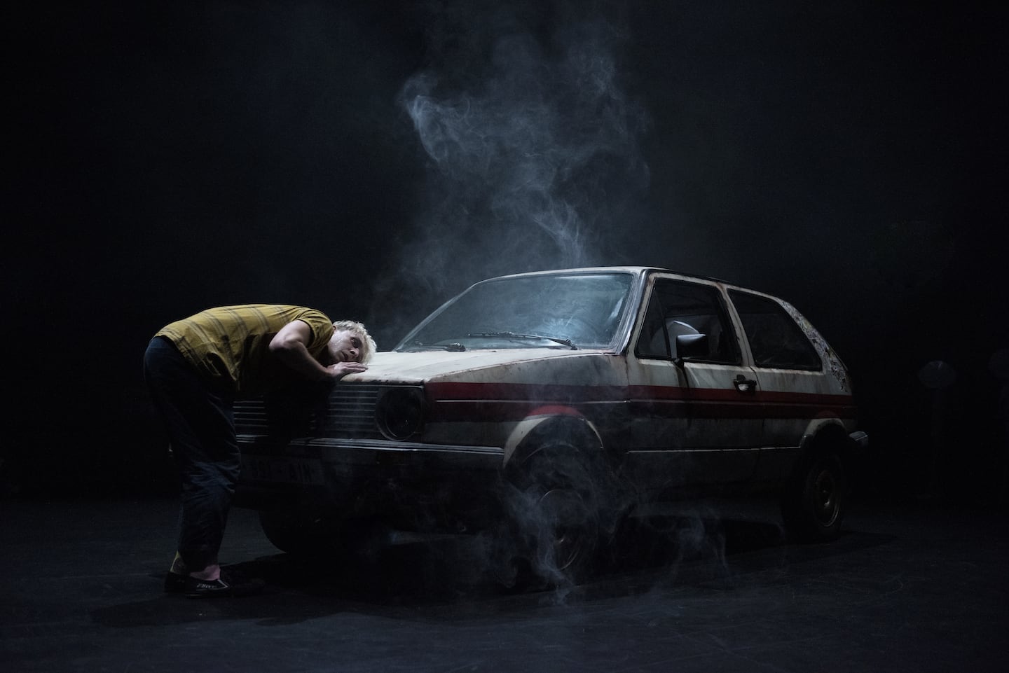 Person leaning on old car with smoke around.