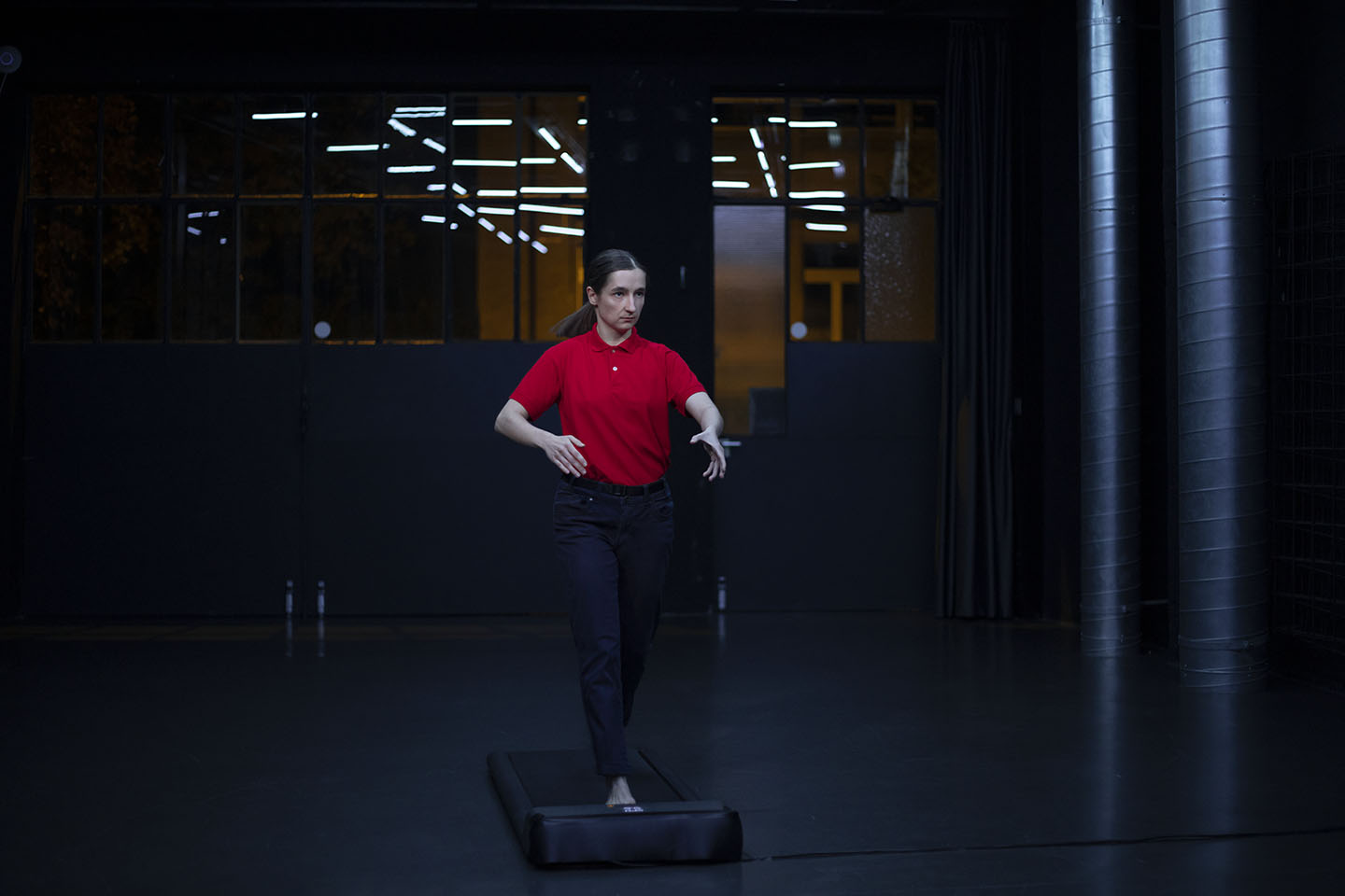 Person balancing on beam indoors with dark background.