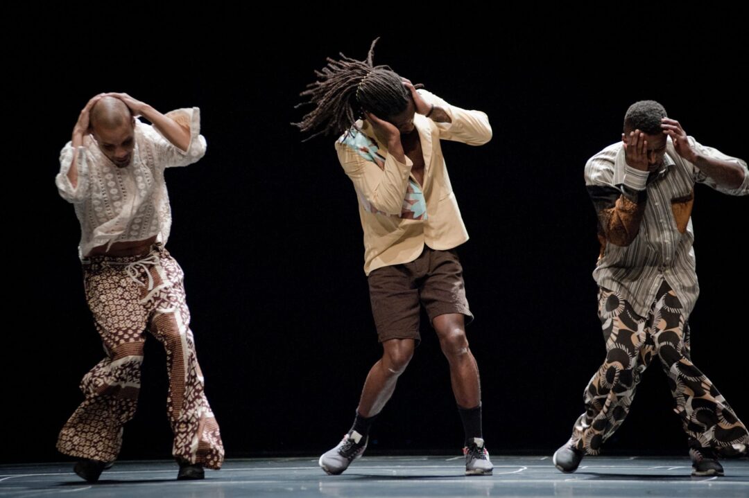 Three dancers performing on stage, holding heads.