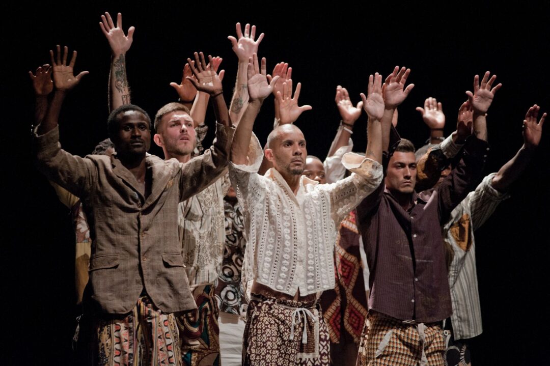 Group of performers raising hands on stage.