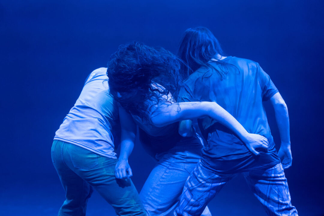 Three people dancing under blue stage light.