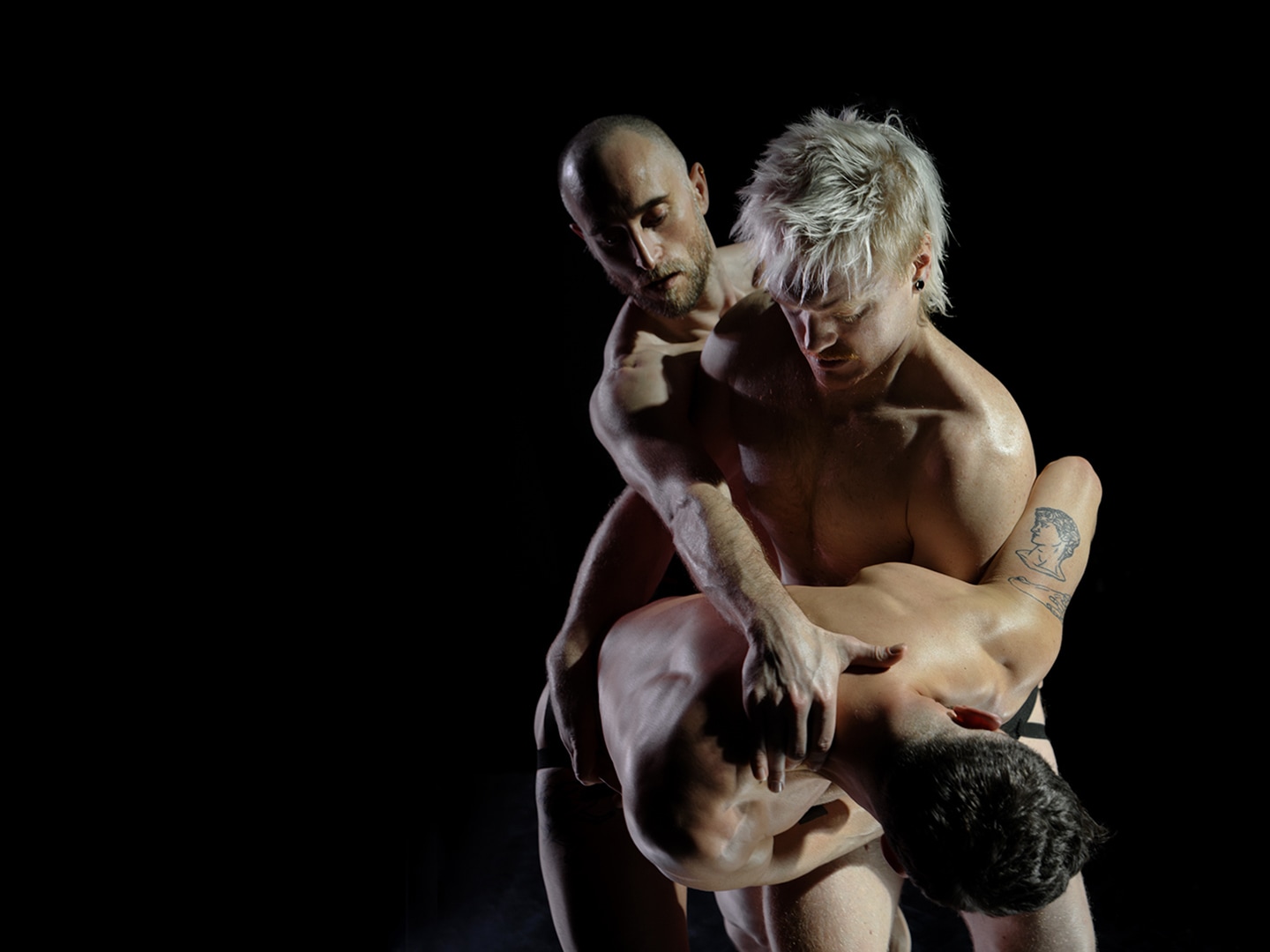 Three dancers perform expressive choreography onstage.