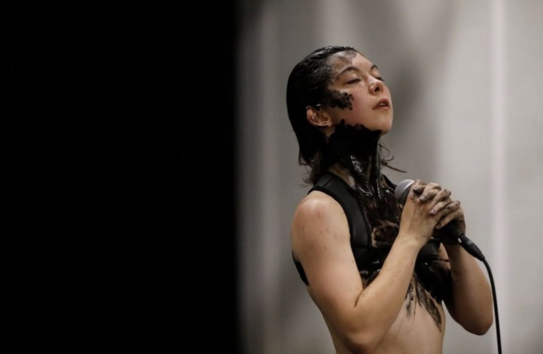 Performer holding microphone, covered in black paint