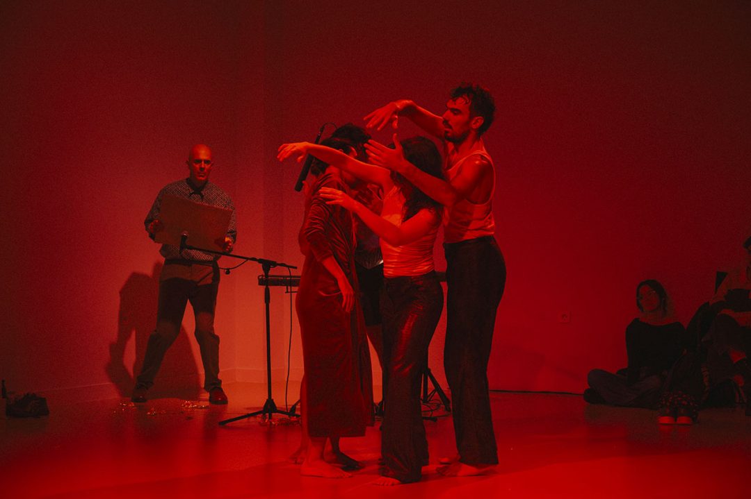 Performers in red-lit room during live art show.