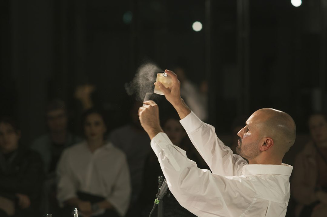Man in white shirt on stage spraying perfume.