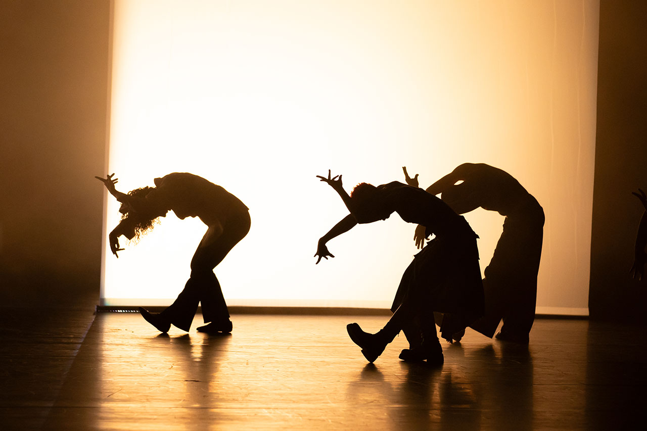Silhouetted dancers perform on stage with backlight.