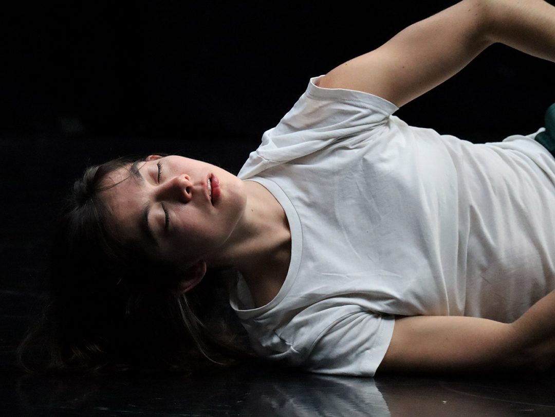 Person lying on stage with closed eyes.