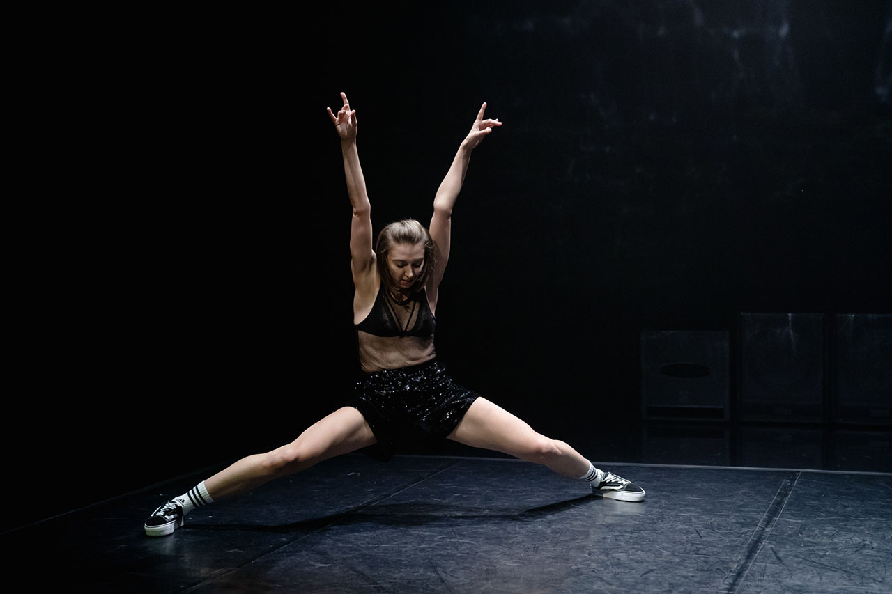 A powerful moment captured mid-performance on a dimly lit stage. Strength and grace combine in a striking contemporary pose.