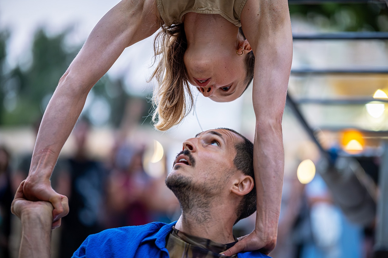 A breathtaking moment of balance and trust during an outdoor acrobatic performance. The duo lock eyes as they hold a gravity-defying pose.