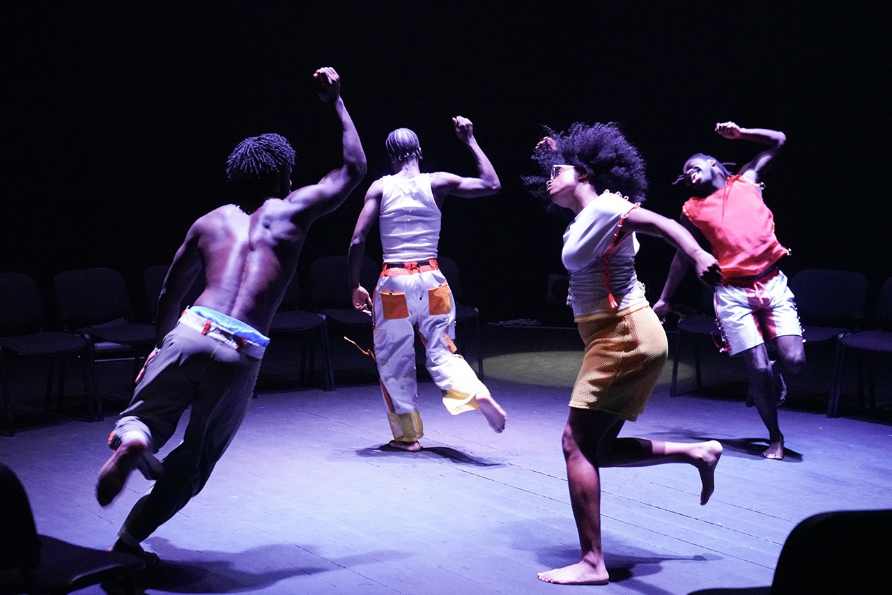 Four performers move with powerful energy under dramatic stage lighting. Their dynamic choreography fills the space with motion and expression.