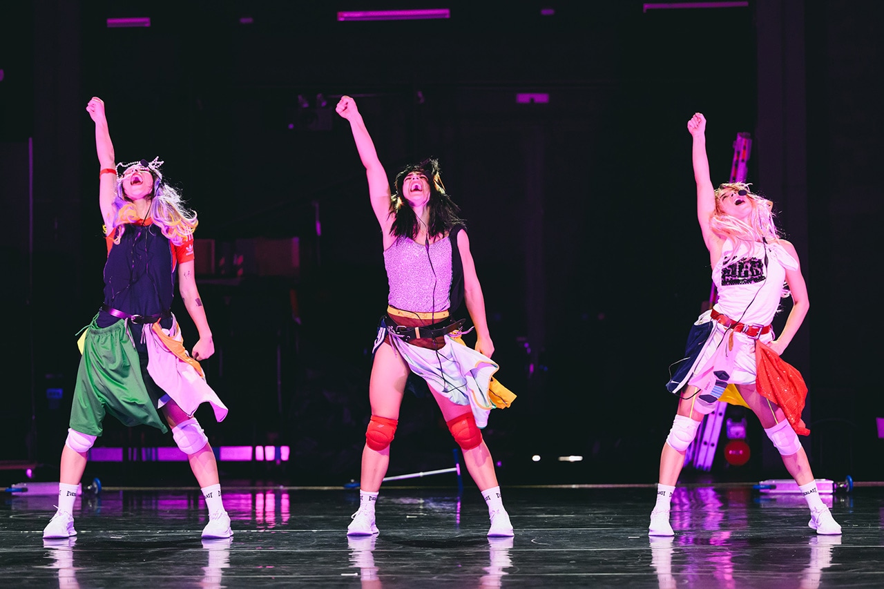 Three performers strike a powerful pose mid-routine. Their high-energy choreography lights up the stage.