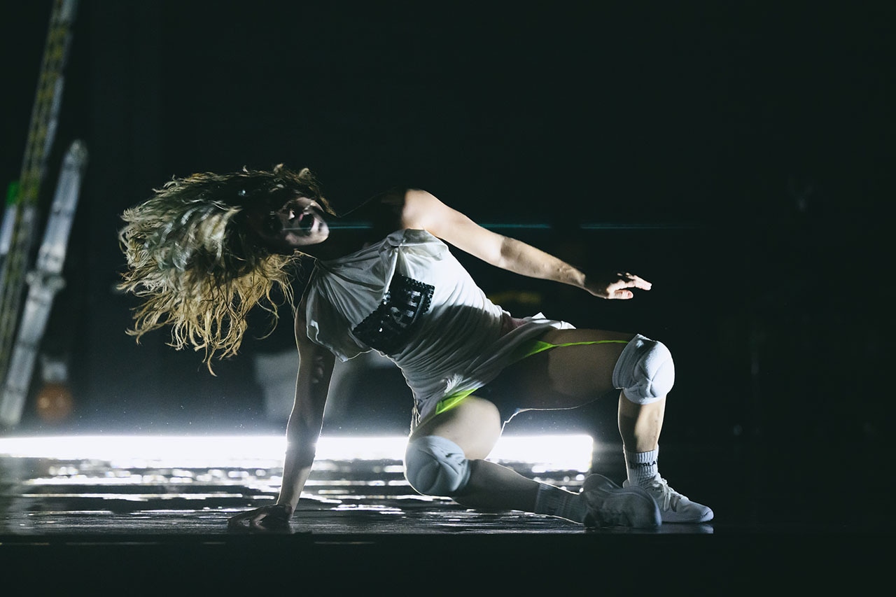 A contemporary dancer moves across a dimly lit stage, captured mid-performance. Dramatic lighting highlights her strength and fluidity.