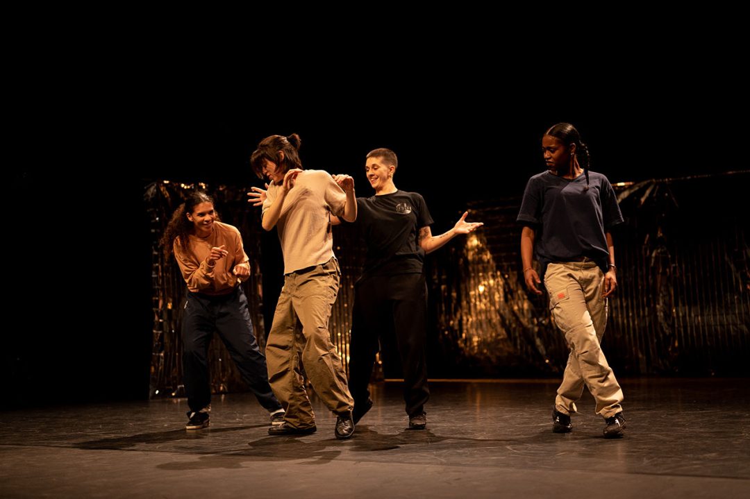 Four dancers performing on a dimly lit stage