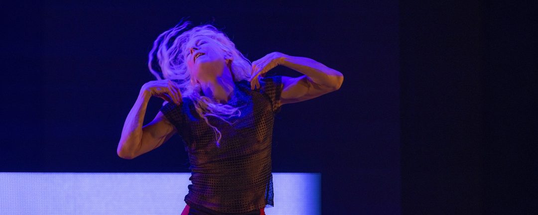 A dancer moves with intensity beneath vivid blue stage lights. Her expressive pose captures a moment of pure emotion in performance.