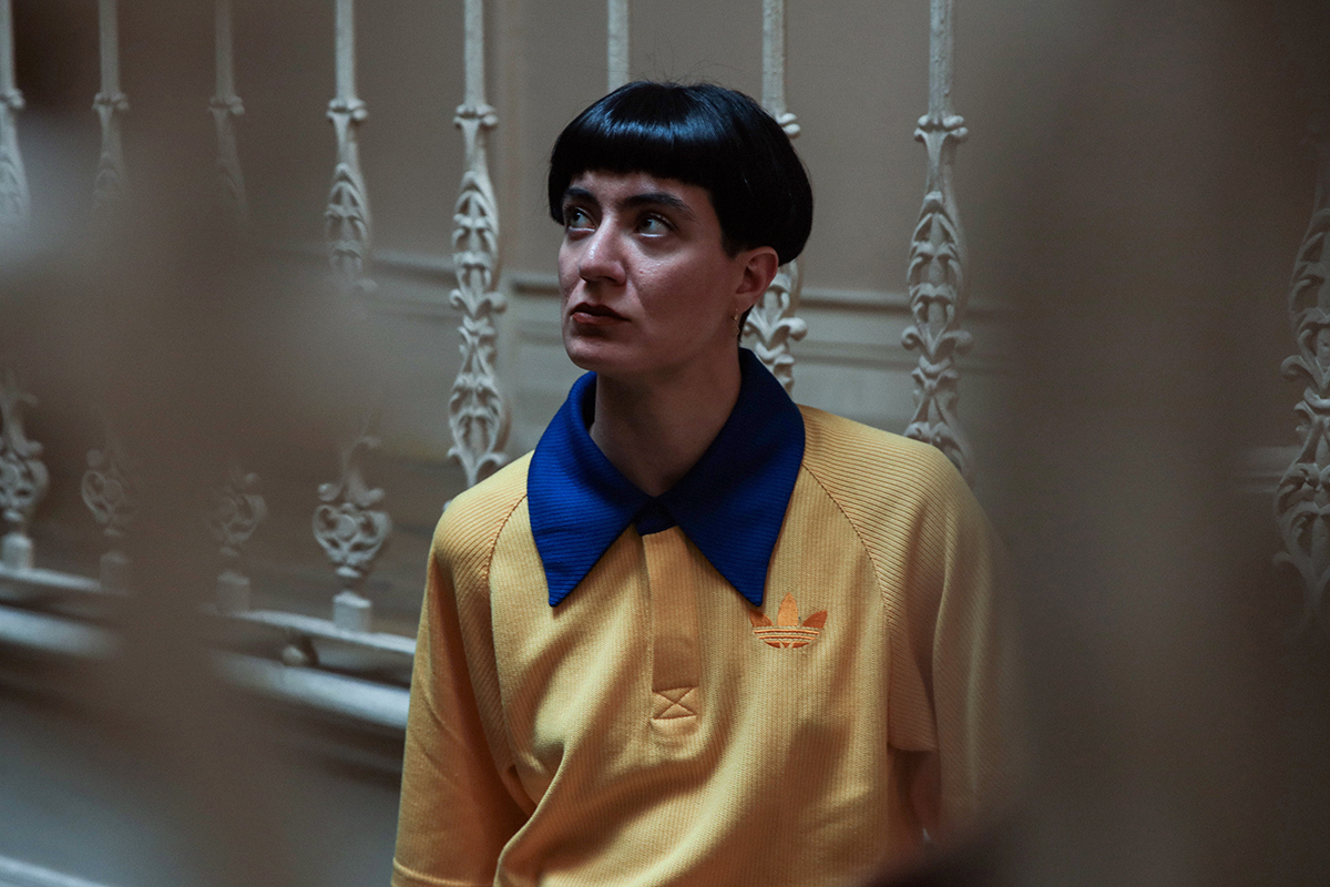 A thoughtful moment captured indoors, framed by ornate railings. The bold colours of the outfit stand out against the muted surroundings.