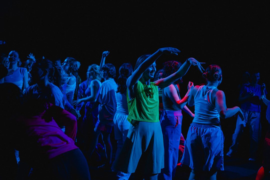 Revellers dance beneath vivid blue and red lighting. The atmosphere is energetic and full of movement.