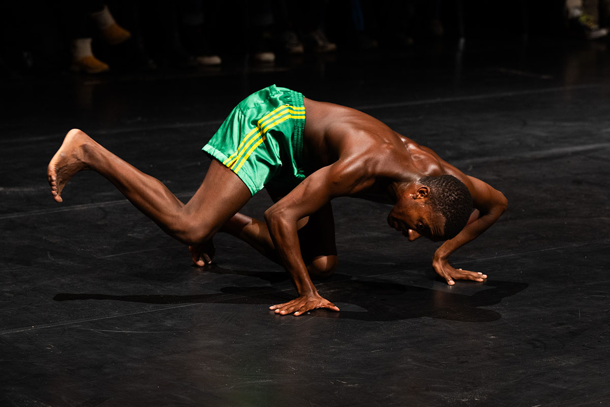 A bare-torsoed man in green football shorts crouches near the ground