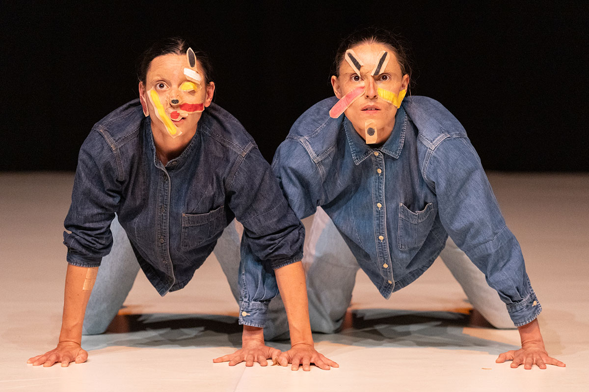 Two performers kneeling wearing abstract tape face masks