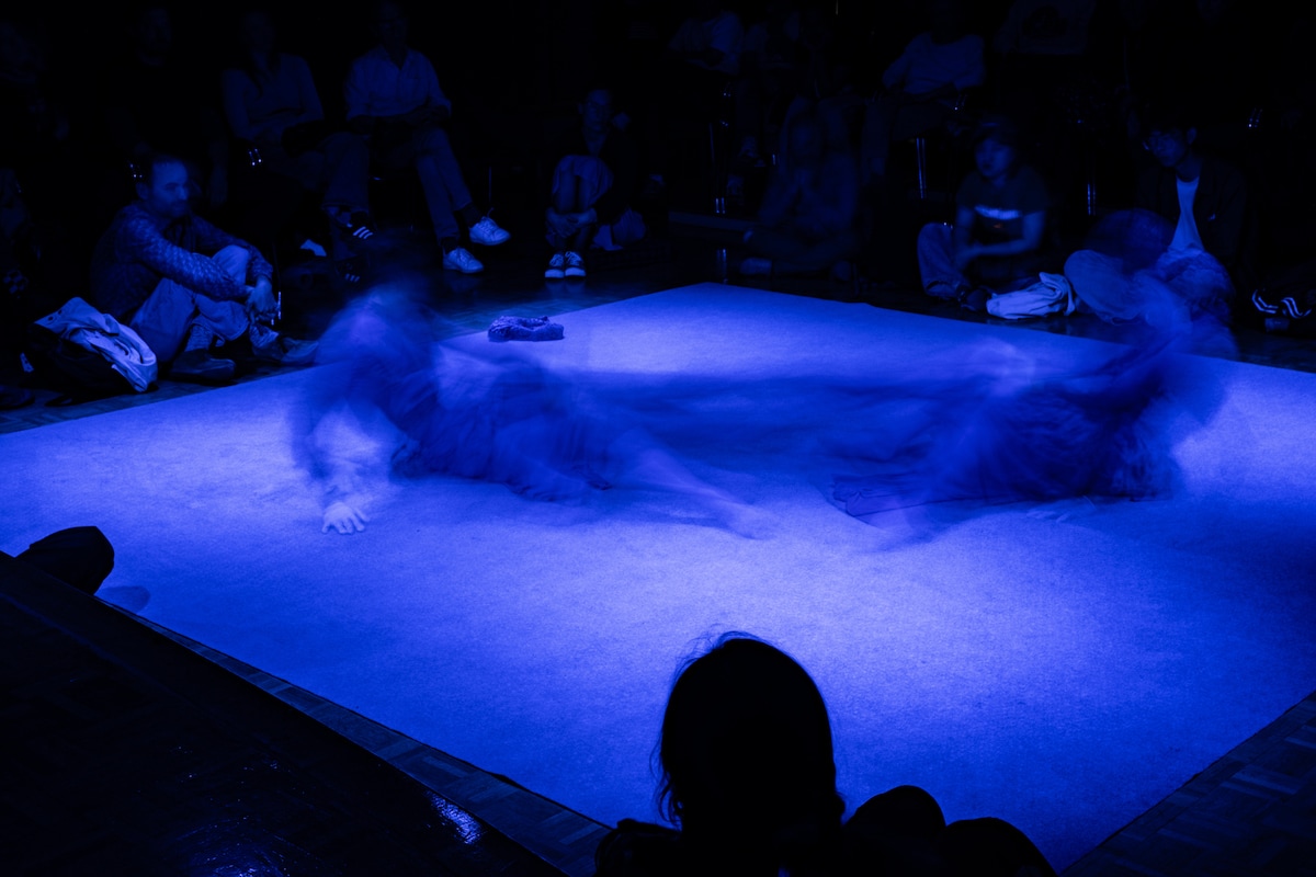 Blurred dancers performing on blue-lit stage surrounded by audience