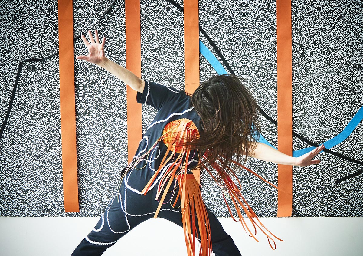 Person dancing before patterned wall with orange stripes