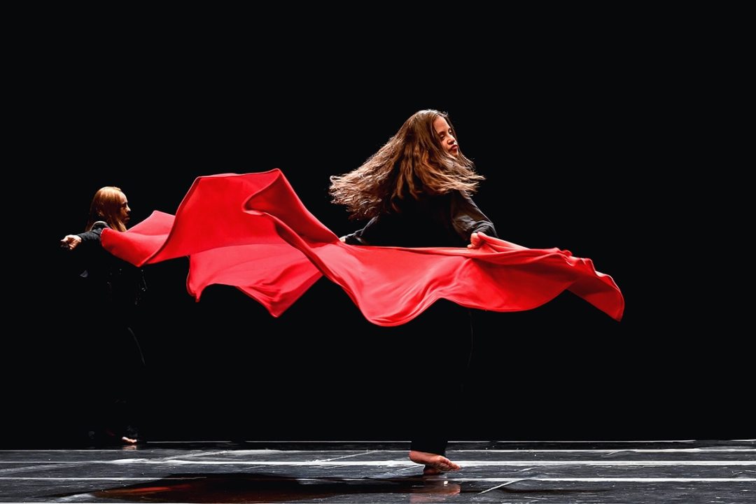 Two dancers twirling red fabric on dark stage