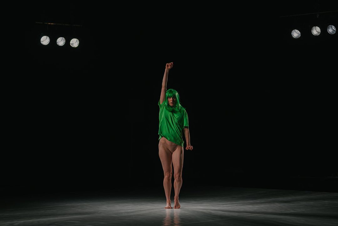 Performer in green wig under stage spotlights