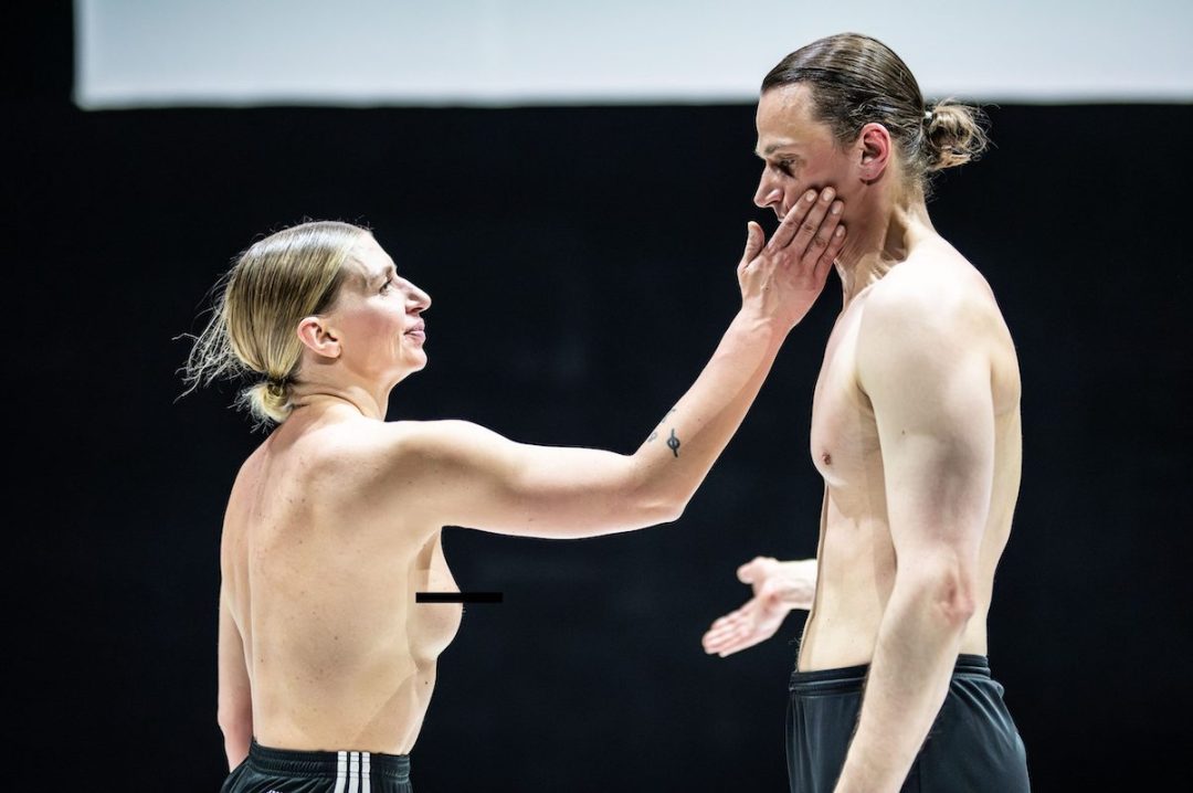 Two topless performers on stage in intense moment