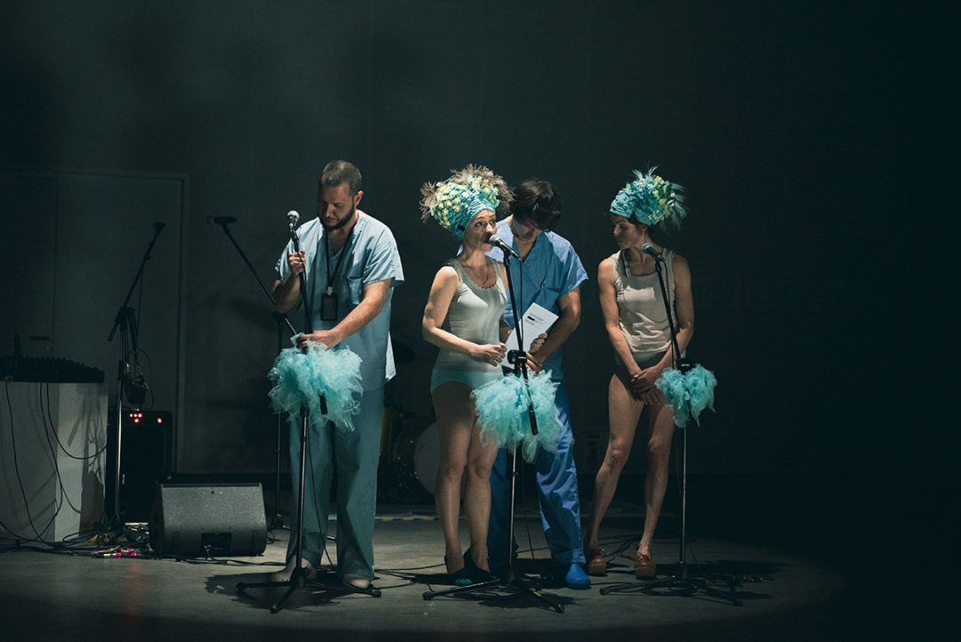 Performers in scrubs and feathered costumes on stage