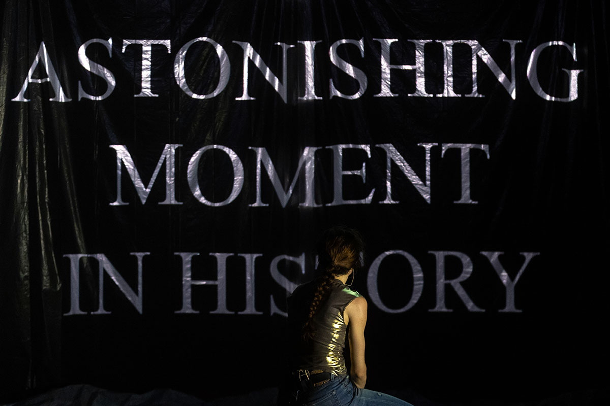 A solitary figure stands before bold words declaring an astonishing moment in history. The dramatic display invites reflection and anticipation.